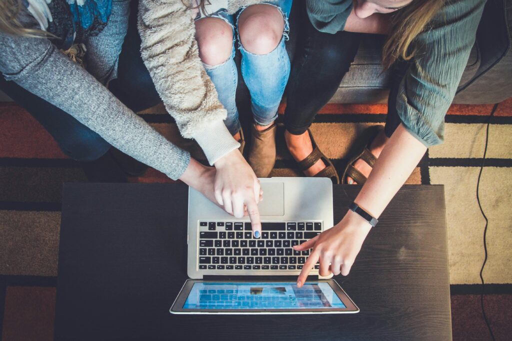 Team members collaborating around a laptop and tablet, representing coordination between design, prototyping, manufacturing, and delivery teams during hardware development.