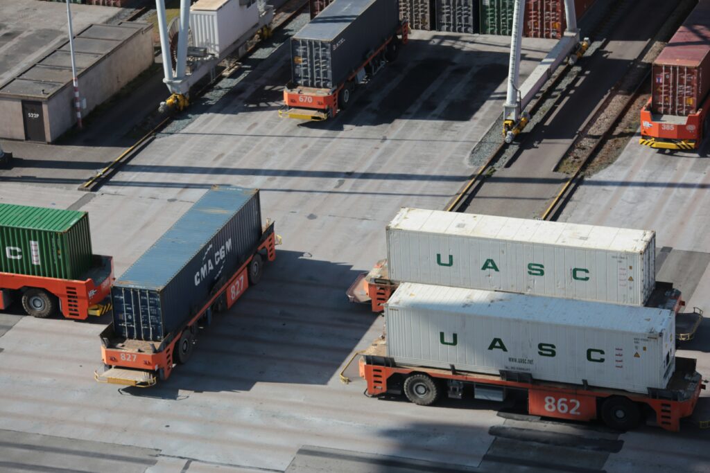 Shipping containers being transported across a logistics yard, representing supply chain coordination and the movement of hardware products from prototype development to production.